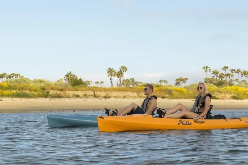 The Image of Two people kayaking on Hobie Revolution 13 kayaks, 2023 model, near a scenic shoreline. - 1