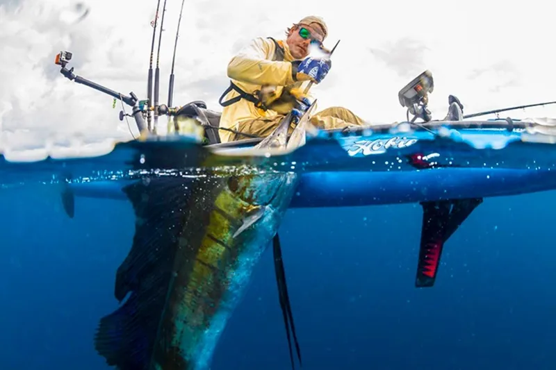 Slide: The Image of Angler on 2023 Hobie Revolution 13 kayak catching a large fish in clear blue water. - 8