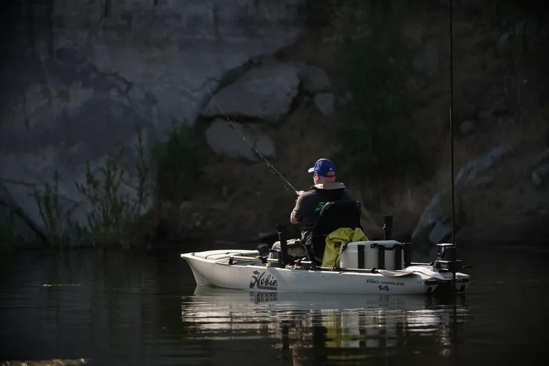 Slide: The Image of Man fishing on a 2022 Hobie MIRAGE PRO ANGLER 14 kayak in a calm lake. - 5