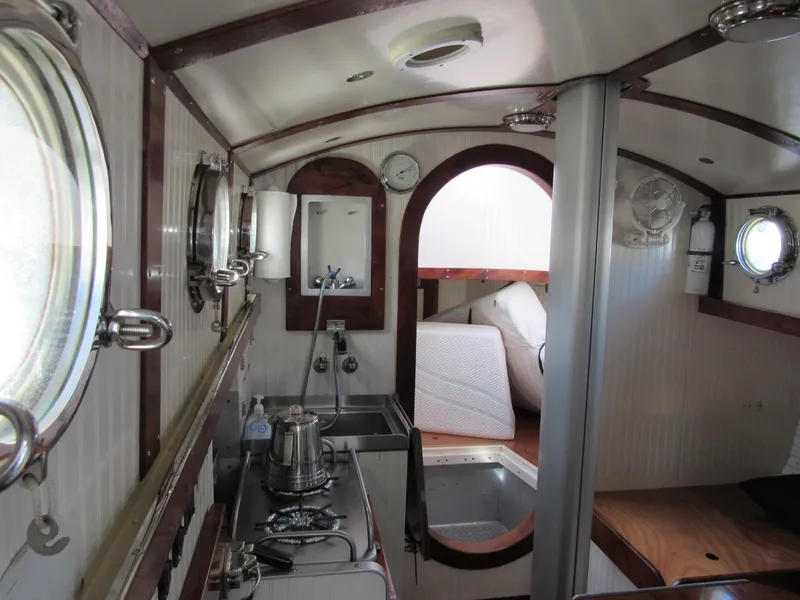 Slide: The Image of Interior of a 2009 Custom Pilothouse Cutter, featuring a compact kitchen and cozy sleeping area. - 16
