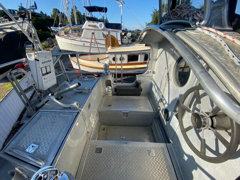 Slide: The Image of 2009 Custom Pilothouse Cutter cockpit with steering wheel and metal deck, docked near other boats. - 42