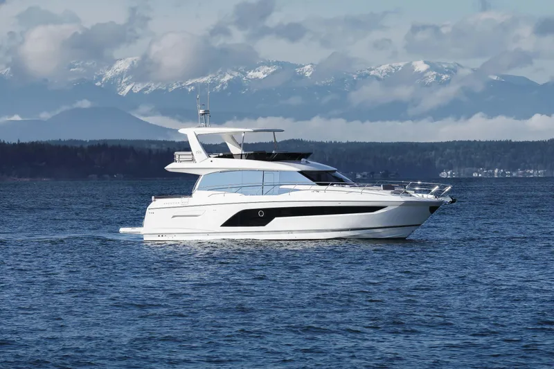 Slide: The Image of 2024 Prestige 590 yacht cruising on a serene lake with mountains in the background. - 3
