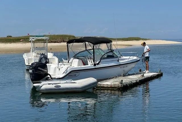 Slide: The Image of 2005 Boston Whaler VENTURA 210 docked on calm water with a person nearby. - 13