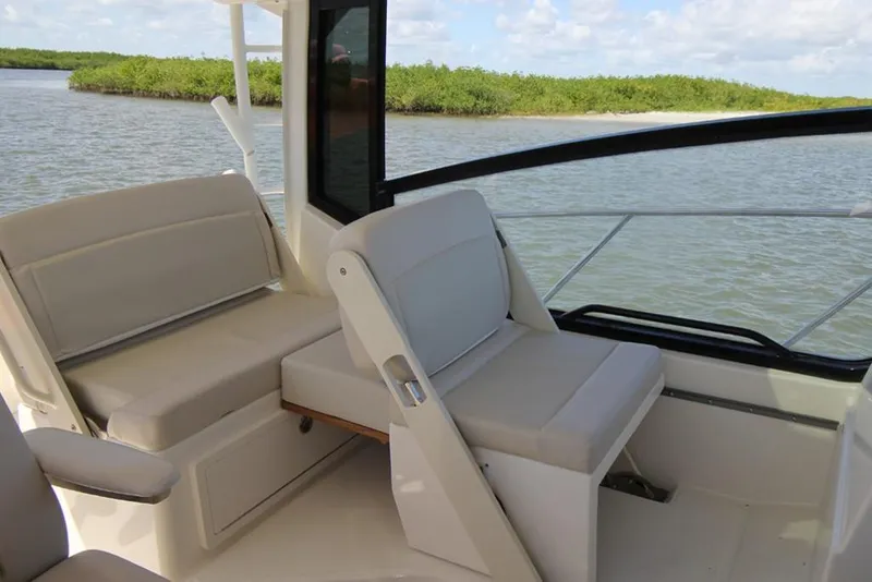 Slide: The Image of 2023 Boston Whaler 325 Conquest boat interior with seating, near water and greenery. - 5