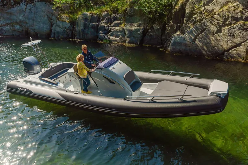 Slide: The Image of 2024 Grand Inflatables G850 boat cruising near rocky shoreline. - 2
