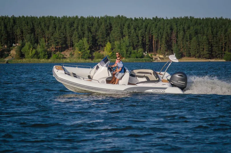 Slide: The Image of 2024 Grand Inflatables G650 boat cruising on a lake with forested shoreline. - 12
