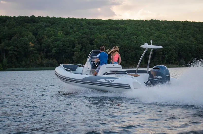 Slide: The Image of 2024 Grand Inflatables G650 boat cruising on a lake with two passengers. - 19