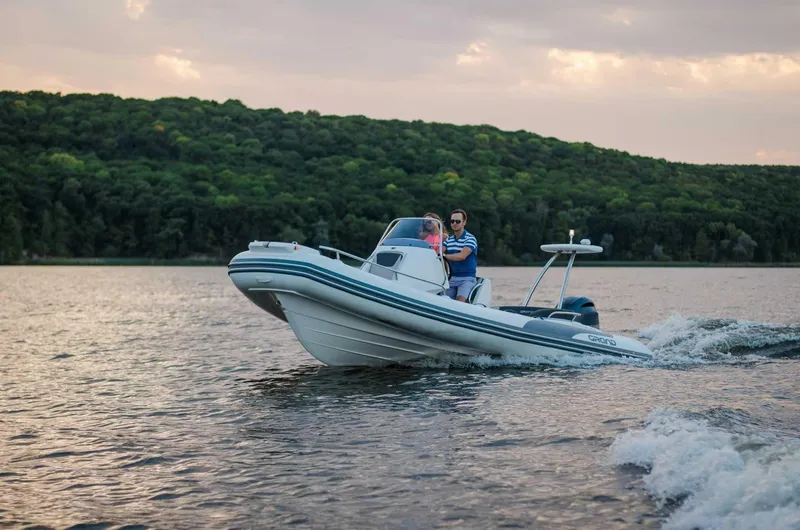 Slide: The Image of 2024 Grand Inflatables G650 boat cruising on a lake with forested hills in the background. - 20