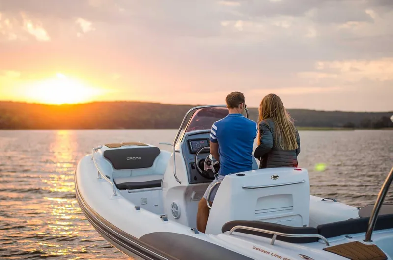 Slide: The Image of 2024 Grand Inflatables G650 boat on a lake at sunset with two people. - 21