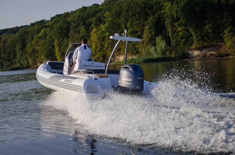 Slide: The Image of 2024 Grand Inflatables G650 boat cruising on a lake with lush green trees in the background. - 23