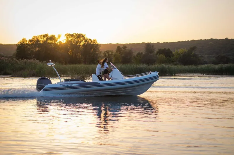Slide: The Image of 2024 Grand Inflatables G650 boat cruising on a lake at sunset. - 28