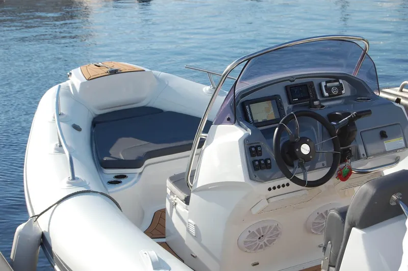 Slide: The Image of 2024 Grand Inflatables G580 boat with modern dashboard and seating, docked on calm water. - 19