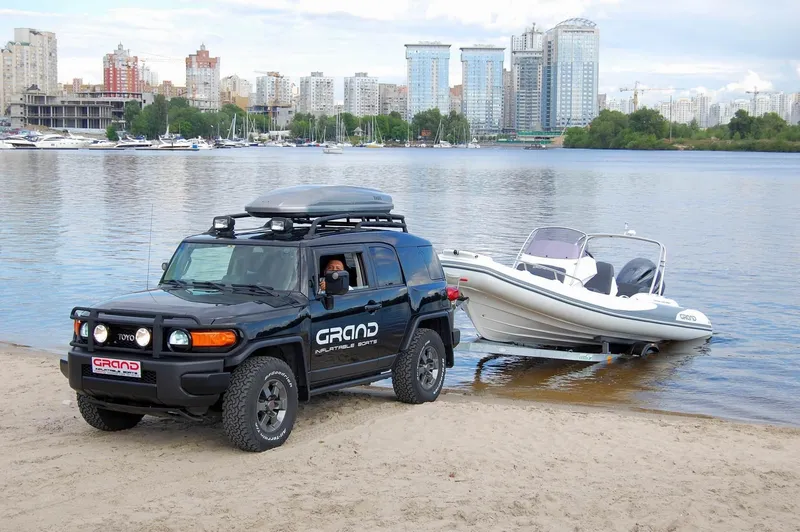 Slide: The Image of SUV towing 2024 Grand Inflatables G580 boat on sandy beach near city waterfront. - 21