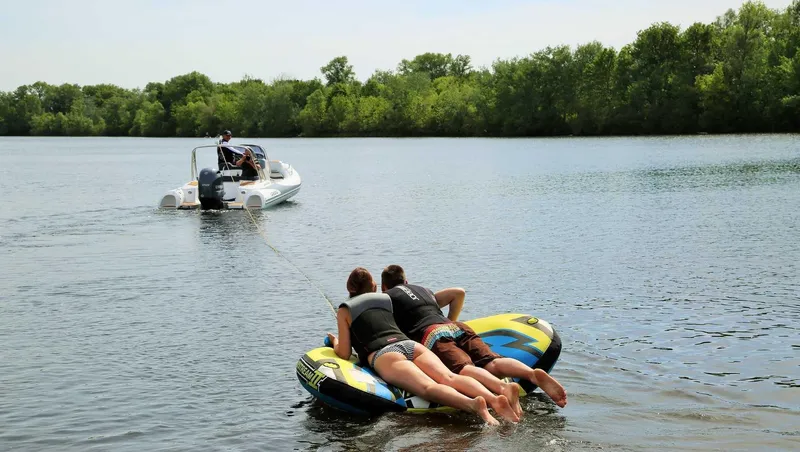 Slide: The Image of People tubing behind a 2024 Grand Inflatables G580 boat on a lake. - 23