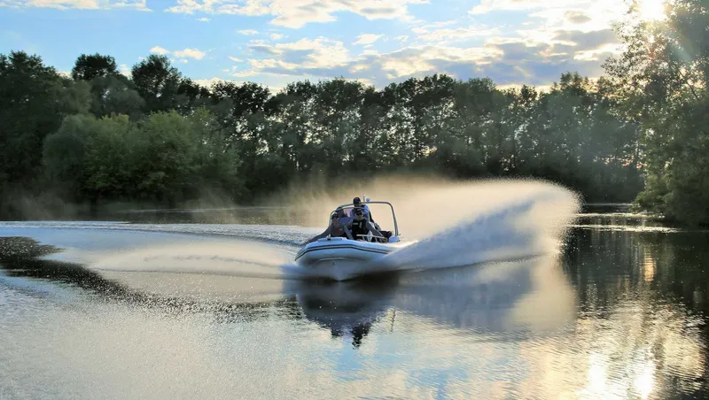 Slide: The Image of 2024 Grand Inflatables G580 boat speeding on a calm lake with trees in the background. - 4