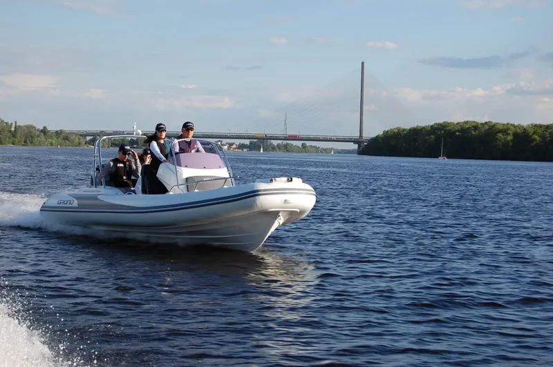 Slide: The Image of 2024 Grand Inflatables G580 boat cruising on a river with a bridge in the background. - 7