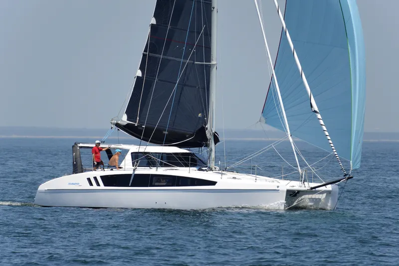 Slide: The Image of 2025 Seawind 1190 Sport catamaran sailing on open water with black and blue sails. - 2