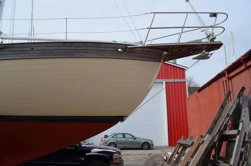 Slide: The Image of 1982 Young Sun Cutter sailboat bow, docked near red building and parked cars. - 46