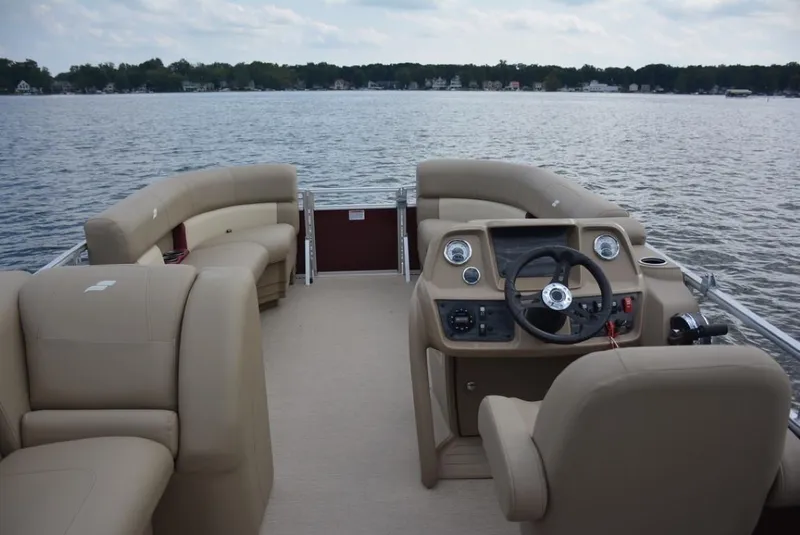 Slide: The Image of 2023 Starcraft LX 20 pontoon boat interior with beige seating on a lake. - 19