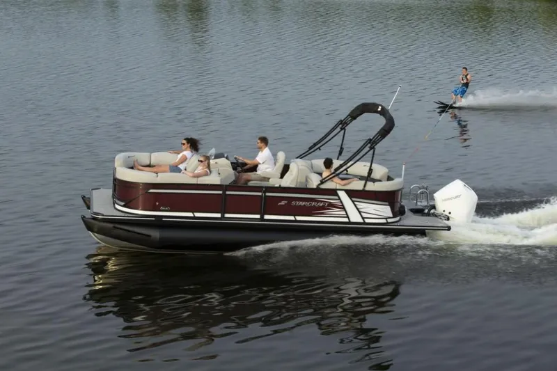 Slide: The Image of 2023 Starcraft SLS 5 pontoon boat cruising with passengers and a water skier. - 10