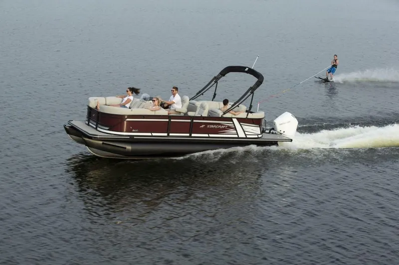 Slide: The Image of 2023 Starcraft SLS 1 pontoon boat cruising with passengers and a water skier. - 2