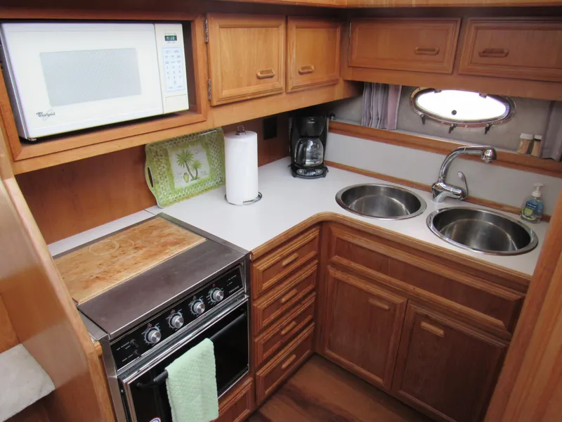 Slide: The Image of 1991 Carver 430 Cockpit Motor Yacht kitchen with microwave, stove, dual sinks, and wooden cabinetry. - 6
