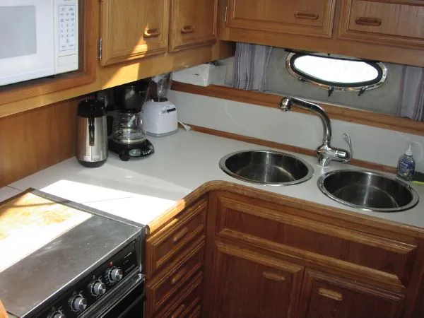 Slide: The Image of 1991 Carver 430 Cockpit Motor Yacht kitchen with dual sinks, stove, and wooden cabinetry. - 7
