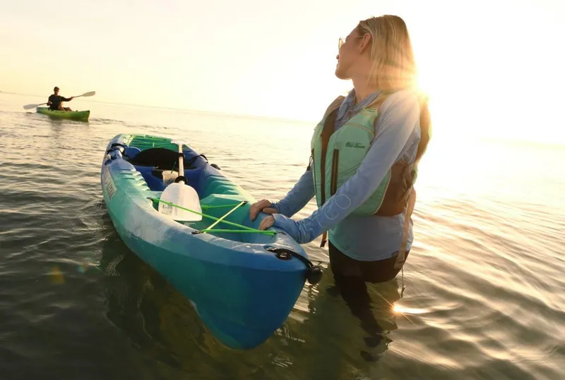 Slide: The Image of Woman with Ocean Kayak Malibu 11.5, 2023 model, in shallow water at sunset. - 2
