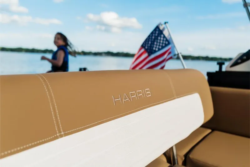 Slide: The Image of 2023 Harris Solstice 250 boat with tan seating and American flag on a lake. - 9