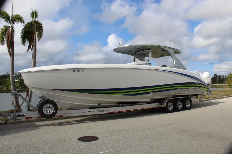 Slide: The Image of 2020 Mystic Powerboats M4200 on trailer, white with blue and green accents, palm trees in background. - 1