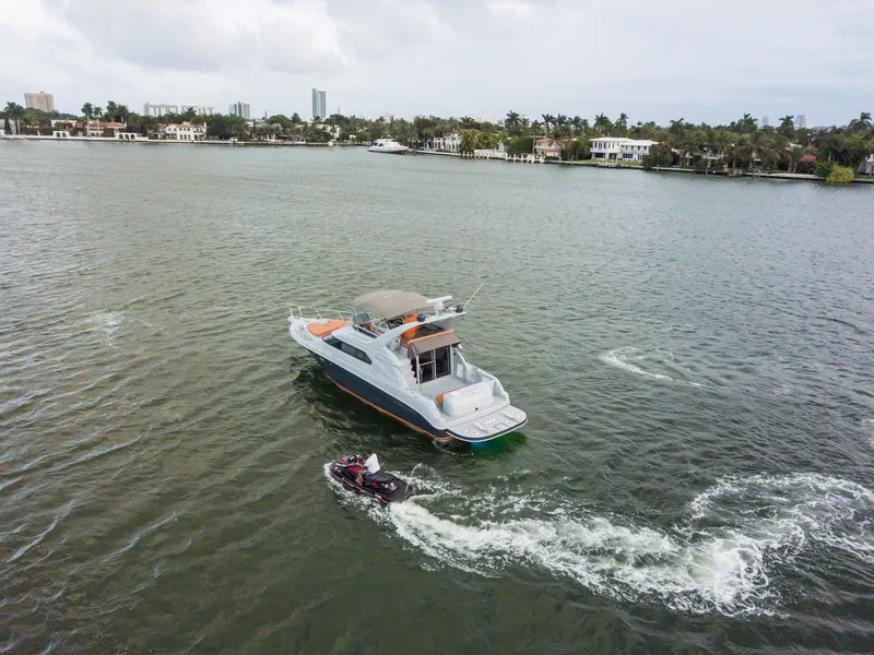 The Image of 2003 Sea Ray Express Bridge yacht cruising with jet ski on a scenic waterway. - 1