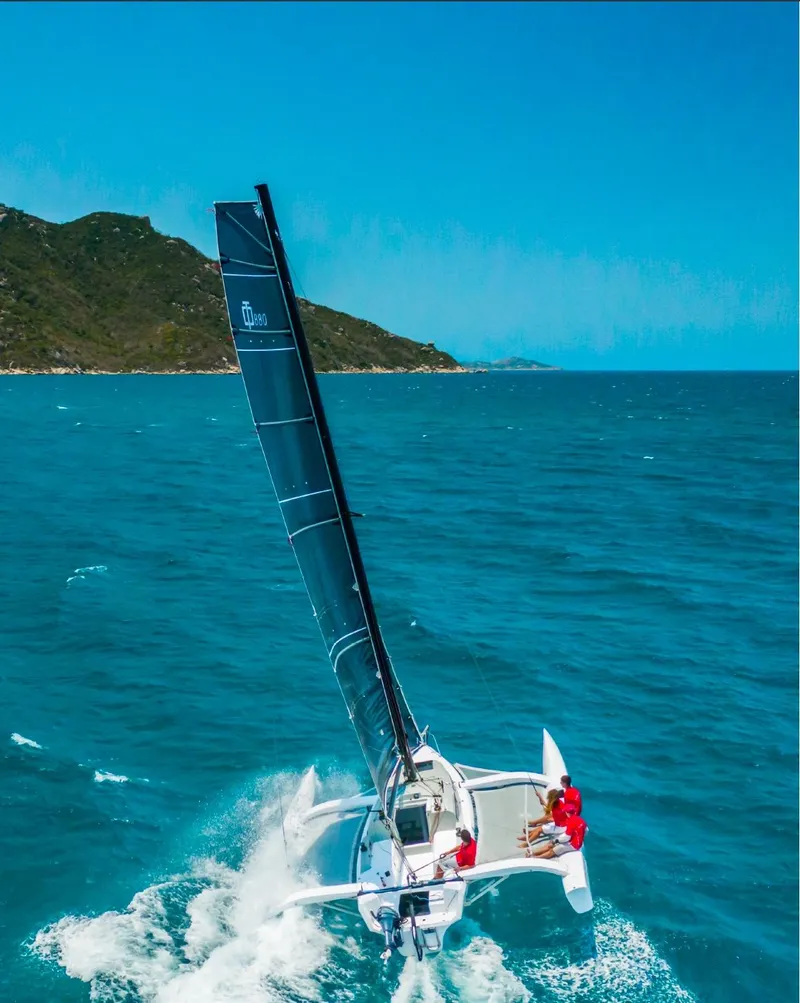 Slide: The Image of Sailing Corsair 880 trimaran gliding on blue ocean near rocky coastline, 2025 model. - 4