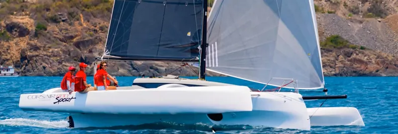 Slide: The Image of 2025 Corsair 880 sailboat on blue water with crew, rocky coastline in background. - 5