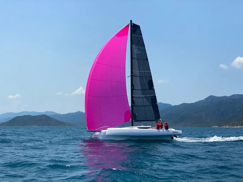 Slide: The Image of Sailing Corsair 880 trimaran with vibrant pink sail on open sea, 2025 model. - 6
