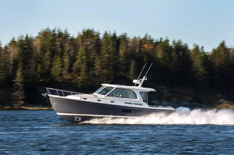 Slide: The Image of 2025 Back Cove 39O cruising on water with forested shoreline in the background. - 2