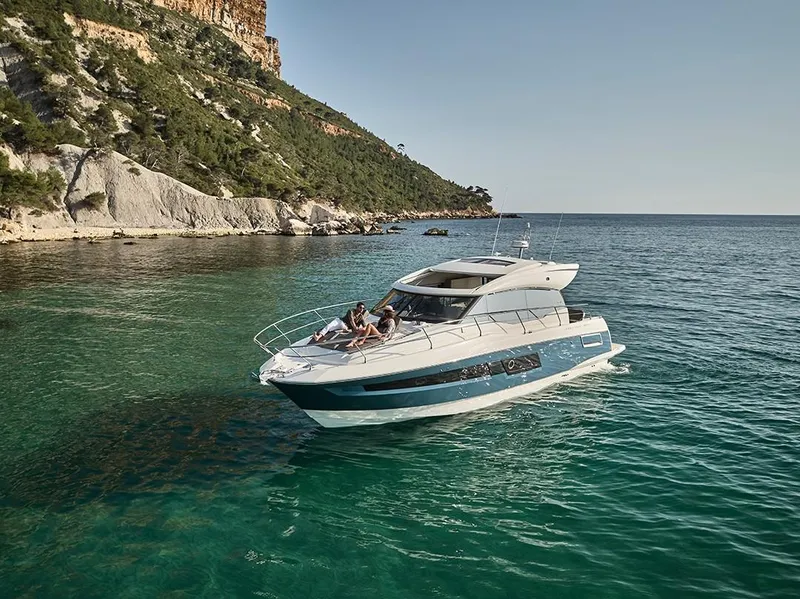 Slide: The Image of 2023 Prestige 460 S yacht cruising in clear blue waters near a rocky coastline. - 2