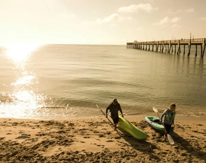 Slide: The Image of Two people with Ocean Kayak Malibu 9.5 kayaks on a sunny beach near a pier. - 5