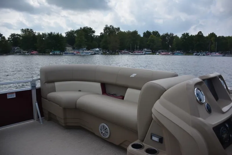 Slide: The Image of 2024 Starcraft LX 18 pontoon boat interior with beige seating on a lake. - 4