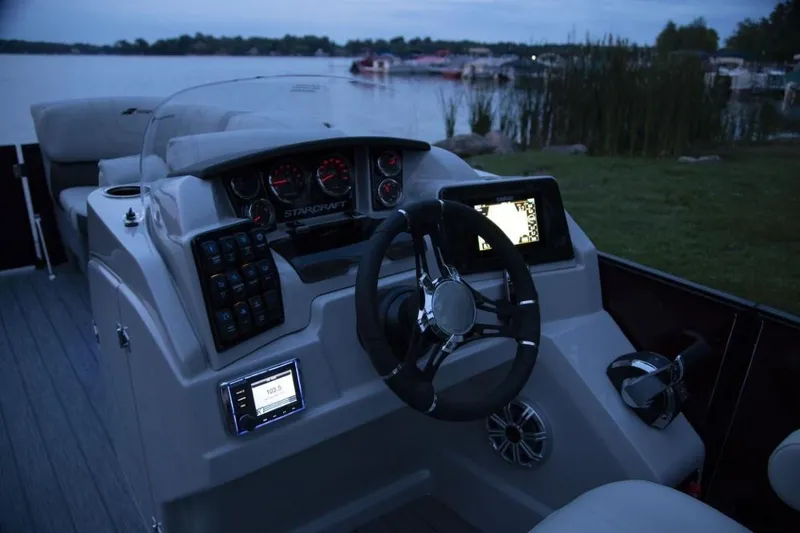 Slide: The Image of 2024 Starcraft SLS 5 boat dashboard with steering wheel and control panels at dusk. - 12