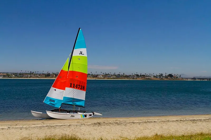Slide: The Image of Colorful 2023 Hobie Cat H16 sailboat on a sandy beach by the water. - 8