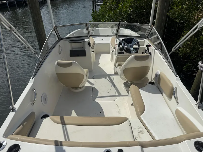 Slide: The Image of 2018 Stingray 191 boat interior with beige seating and steering wheel, docked by water. - 10