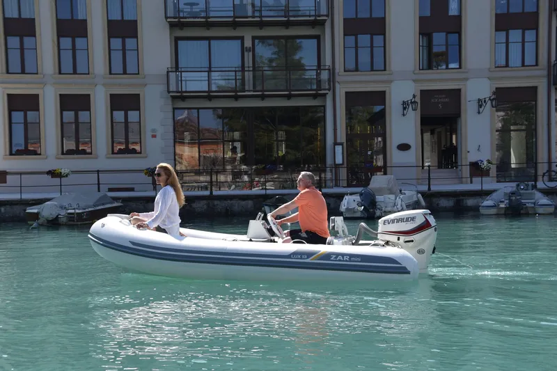 Slide: The Image of 2023 ZAR Mini LUX 13 boat cruising on clear water near a waterfront building. - 3