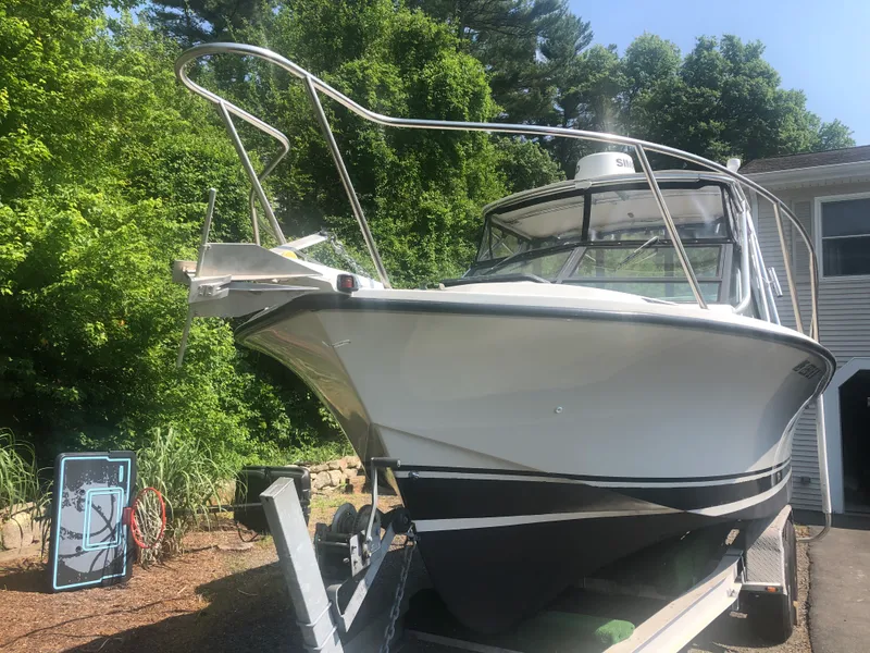 Slide: The Image of 1990 Rampage 24 boat on trailer, surrounded by greenery and a house. - 2