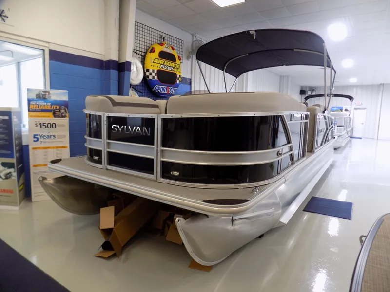 Slide: The Image of 2023 Sylvan L5 DLZ Bar pontoon boat displayed indoors with promotional banners. - 3