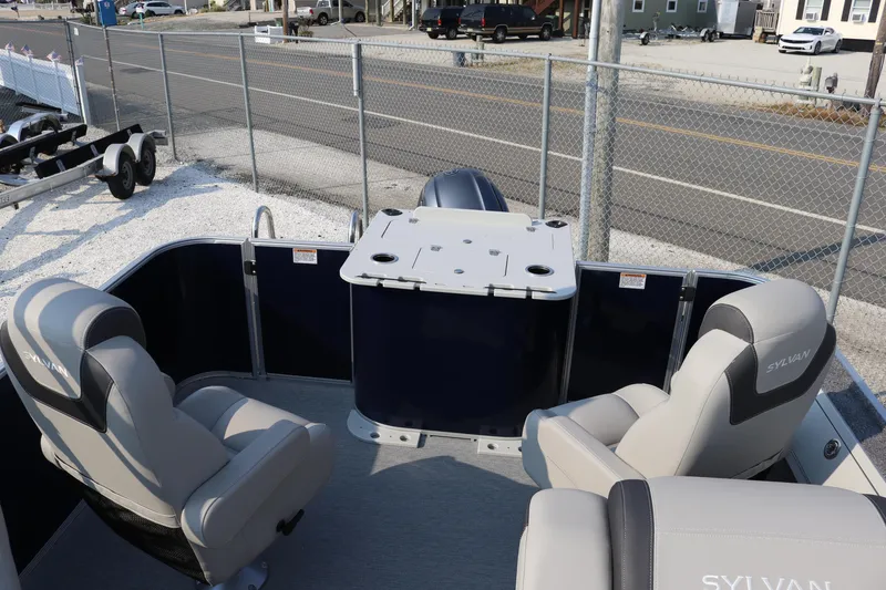Slide: The Image of 2023 Sylvan L3 Party Fish boat interior with seating and table, parked near a fence. - 8