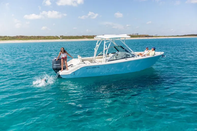 Slide: The Image of 2024 Cobia 240 Dual Console boat on clear blue water with people enjoying the sun. - 2
