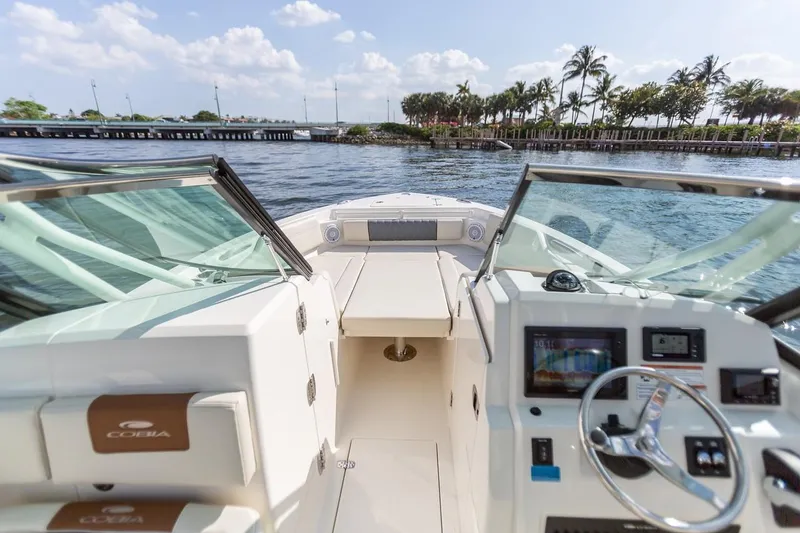 Slide: The Image of 2024 Cobia 240 Dual Console boat interior with open water and palm trees in the background. - 8