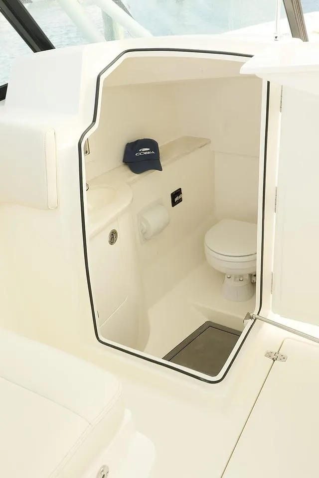 Slide: The Image of 2024 Cobia 280 Dual Console boat interior bathroom with toilet and storage shelf. - 14