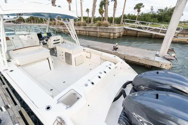 Slide: The Image of 2024 Cobia 330 Dual Console boat docked, featuring spacious deck and twin outboard engines. - 7