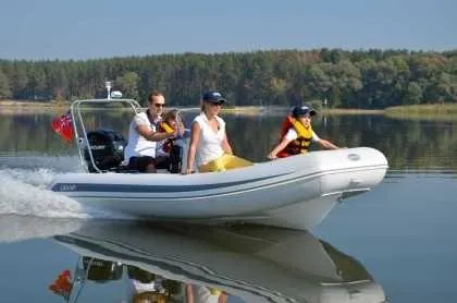 Slide: The Image of 2024 Grand Inflatables S420 boat cruising on a calm lake with three passengers. - 2
